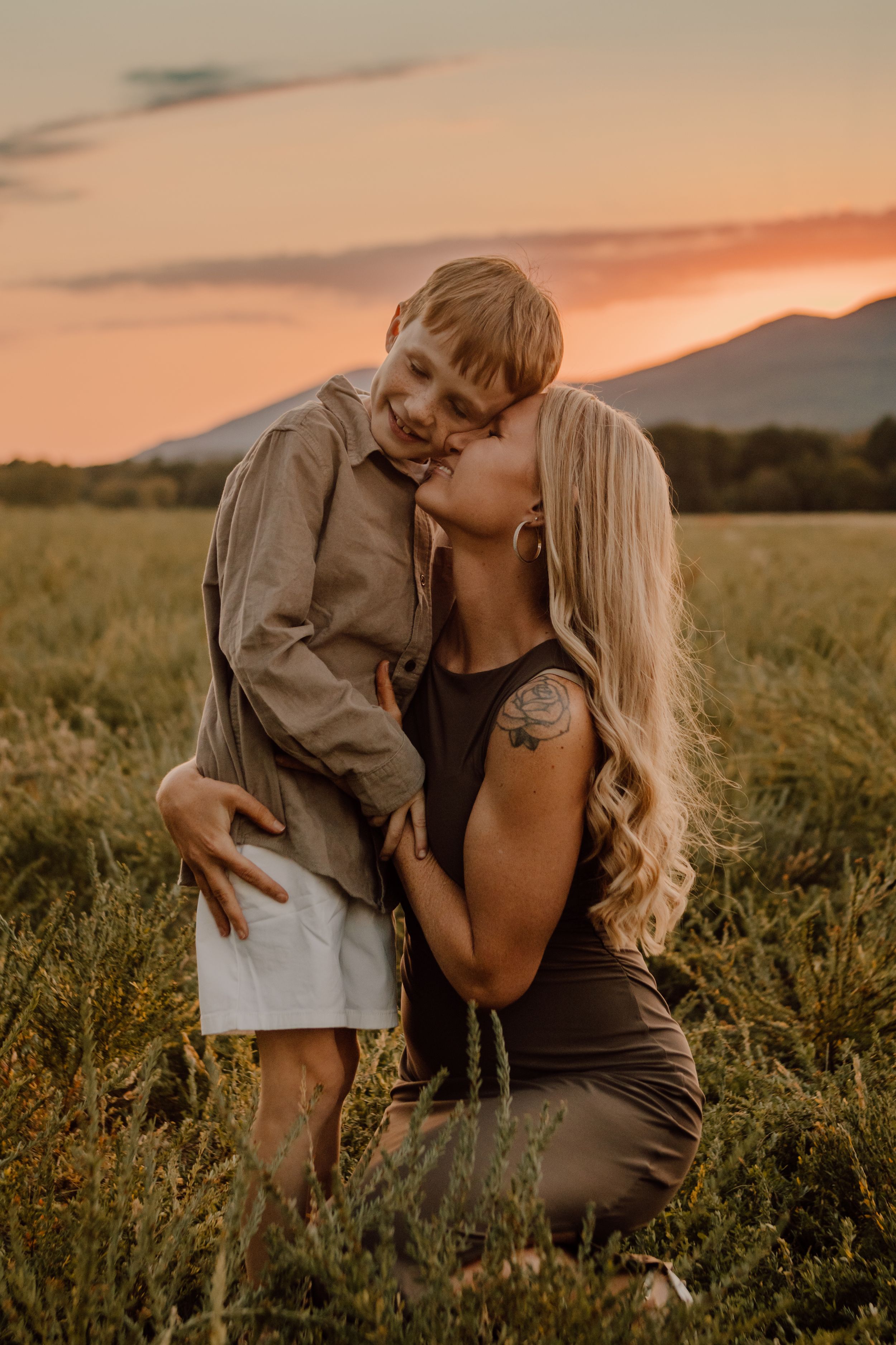 Intimate sunset portrait of mother and child in golden field with mountains.