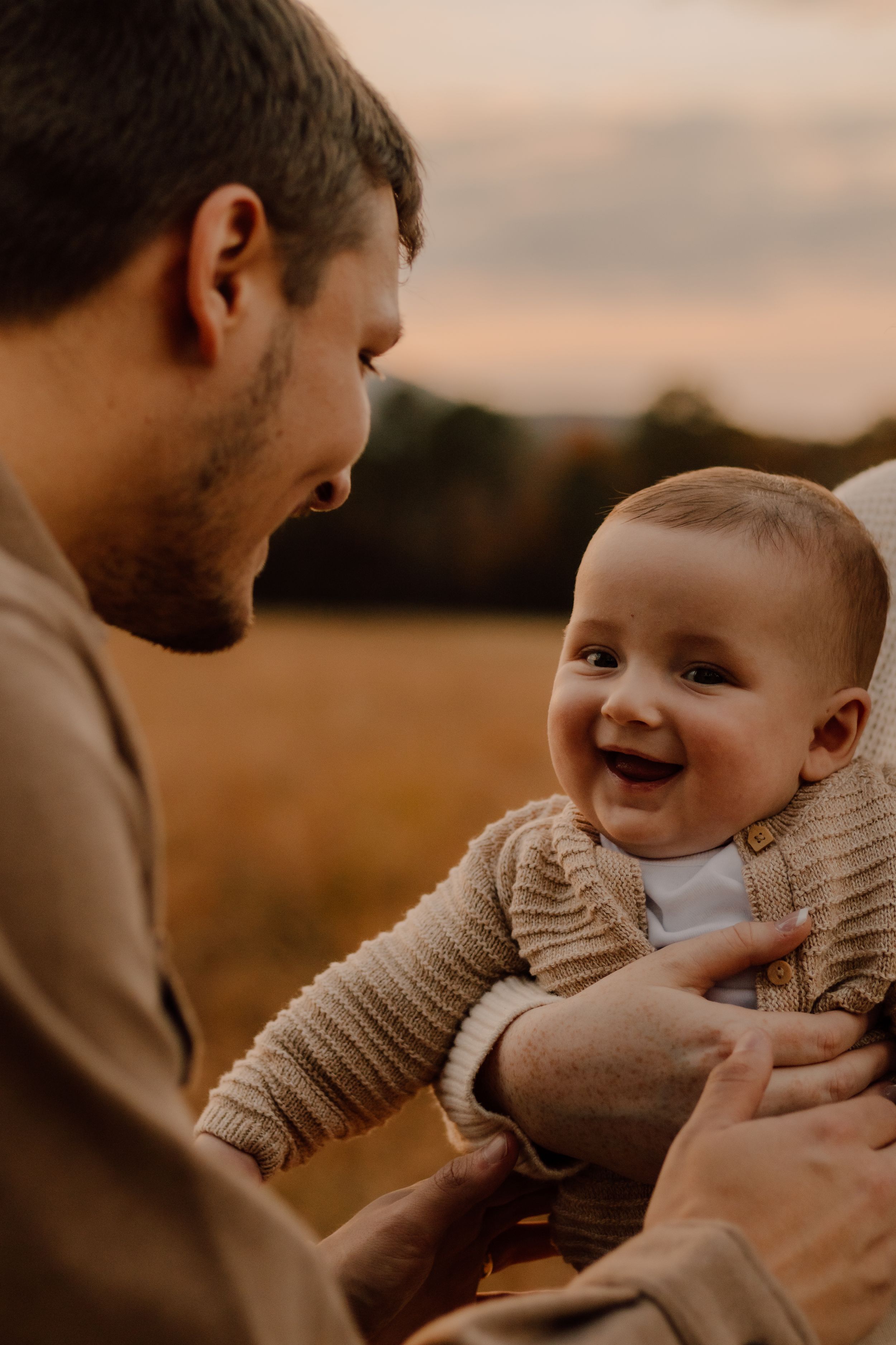 Candid moment between parent and laughing baby in warm sunset light.