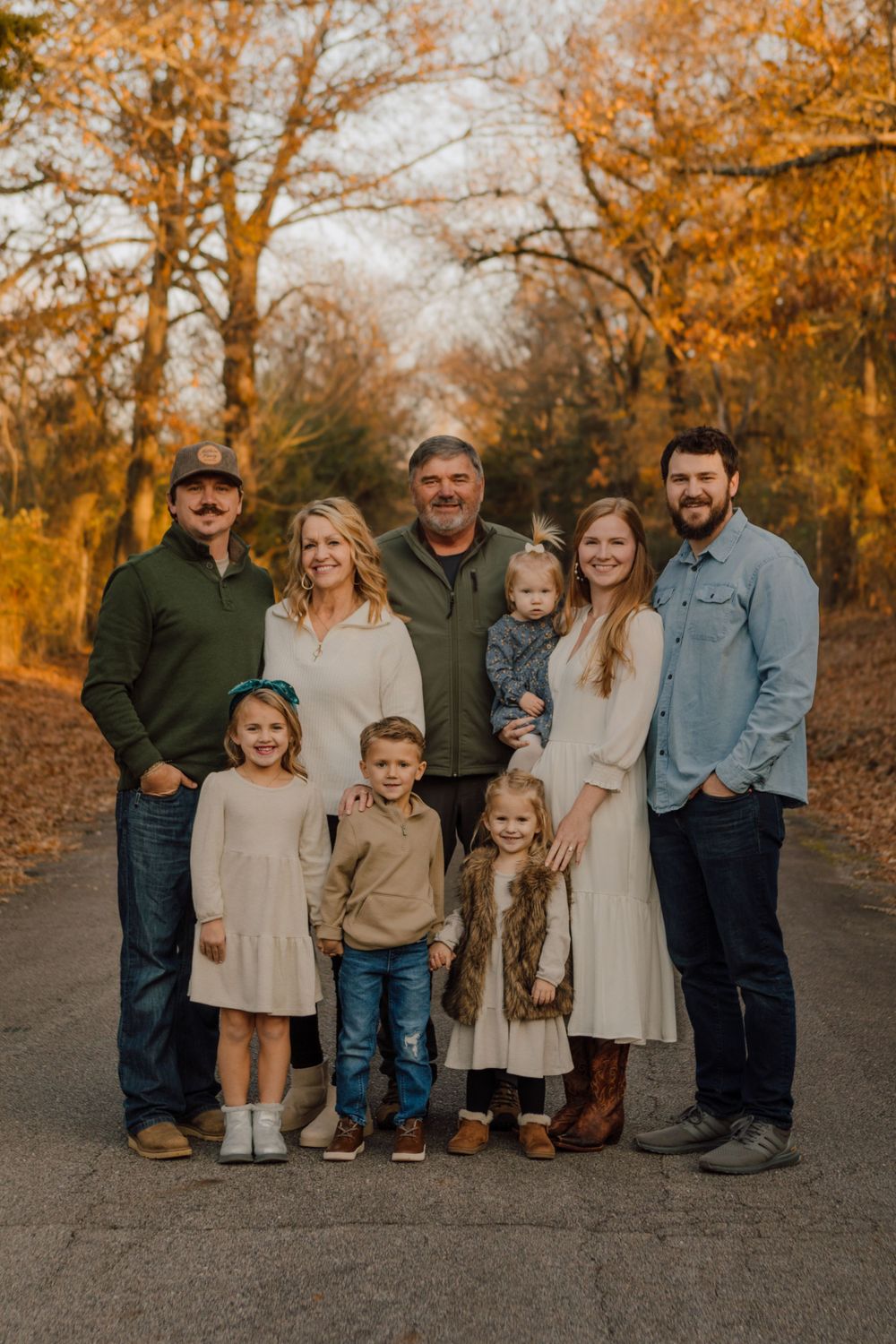 Fall family portrait of multi-generational group in autumn colors on tree-lined path.