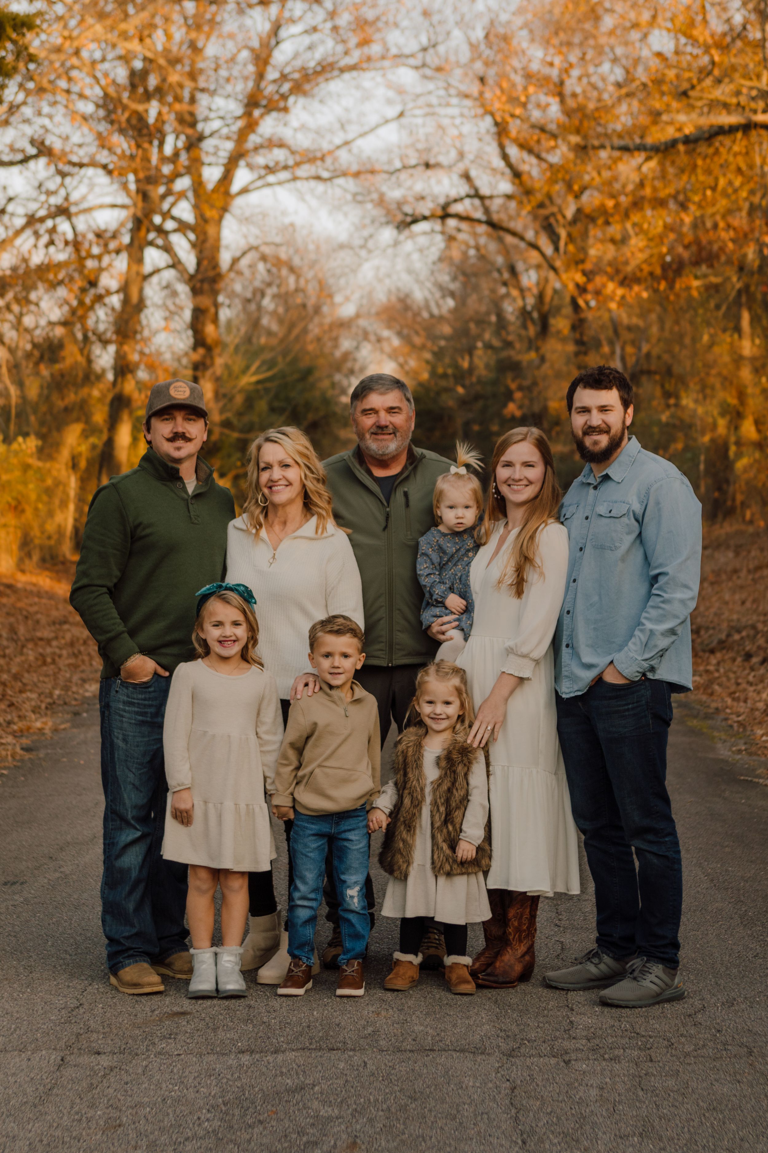 Fall family portrait of multi-generational group in autumn colors on tree-lined path.