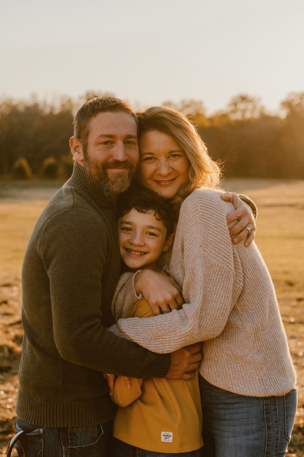 Intimate family portrait captured during golden hour in an autumn field.