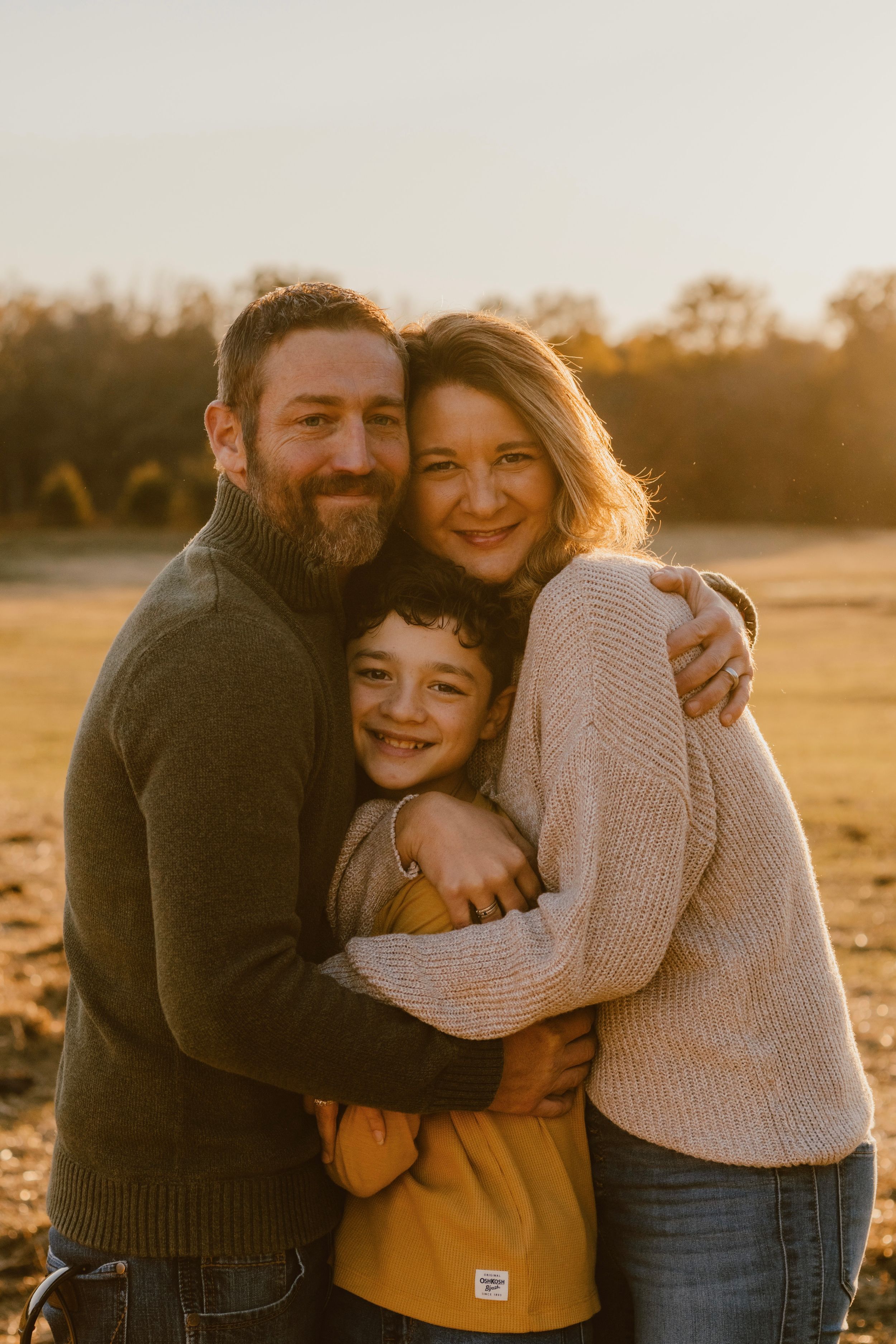 Intimate family portrait captured during golden hour in an autumn field.