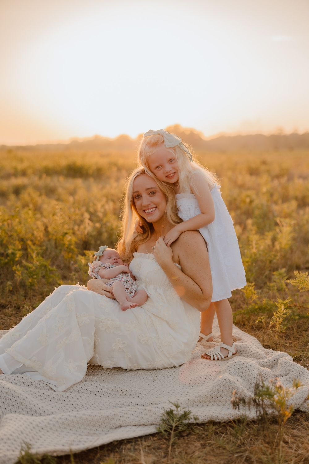 A joyful family moment captured at sunset in a golden field with a blanket spread on the grass.