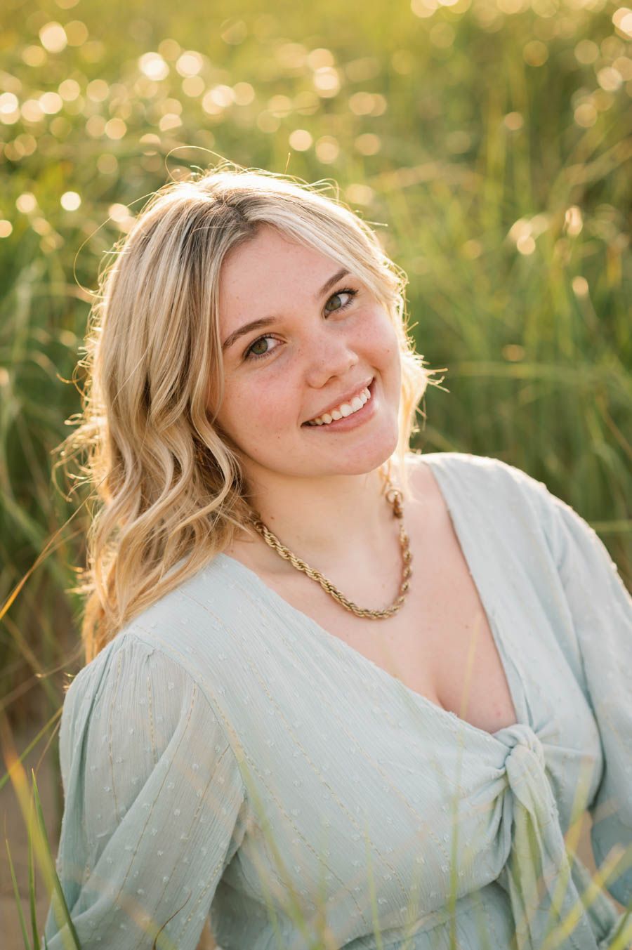 Portrait series in golden sunlit meadow with a light blue dress and braided hairstyle against a dreamy summer backdrop.