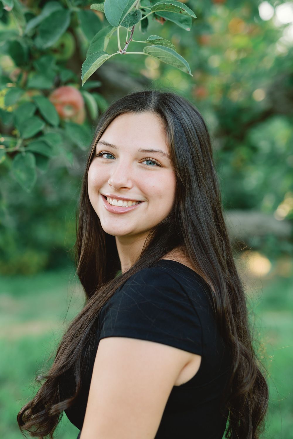 Four outdoor headshots show a person with long dark hair in a black top posing against lush green foliage.