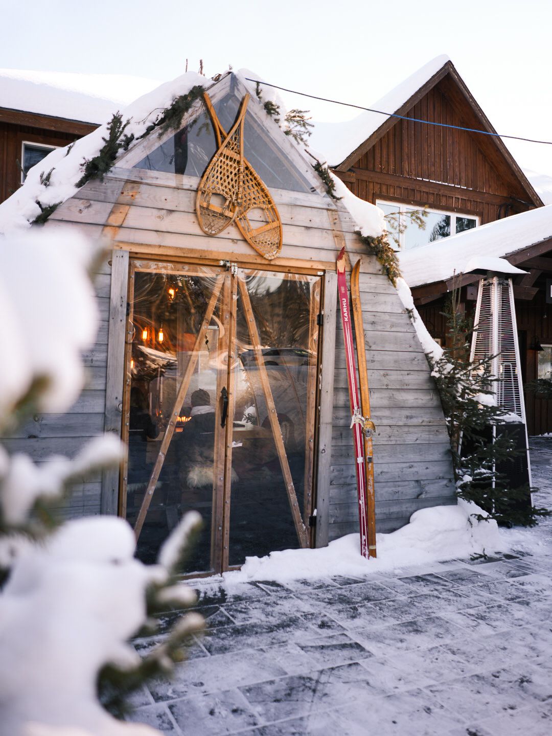 Snow-covered wooden cabin with glass windows and rustic architecture in winter setting.