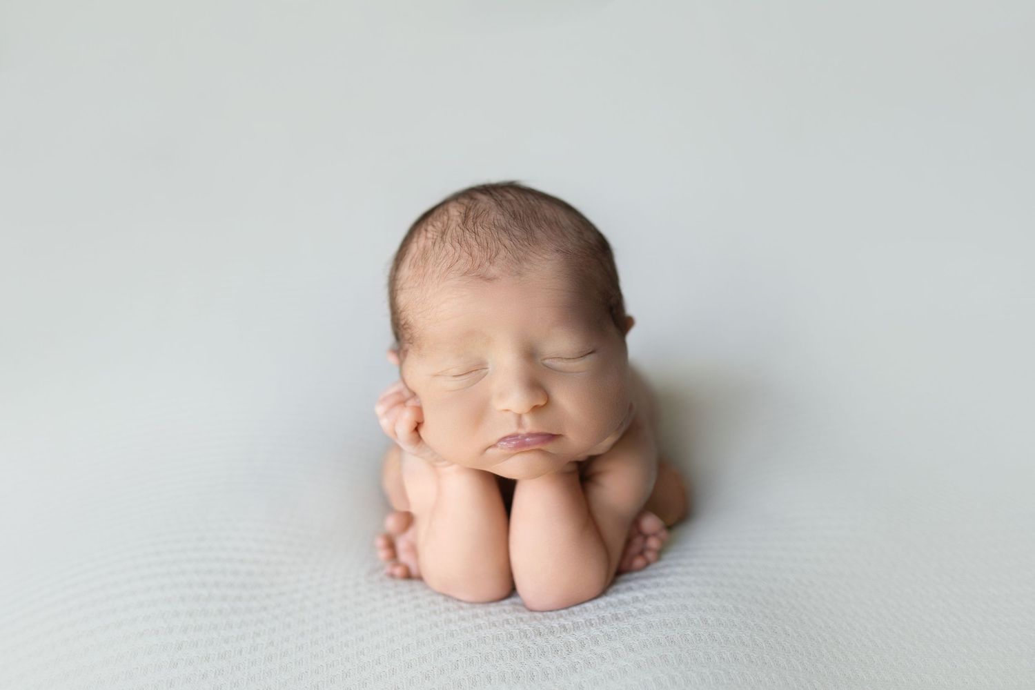 Sleeping newborn positioned on plain backdrop in fetal pose.