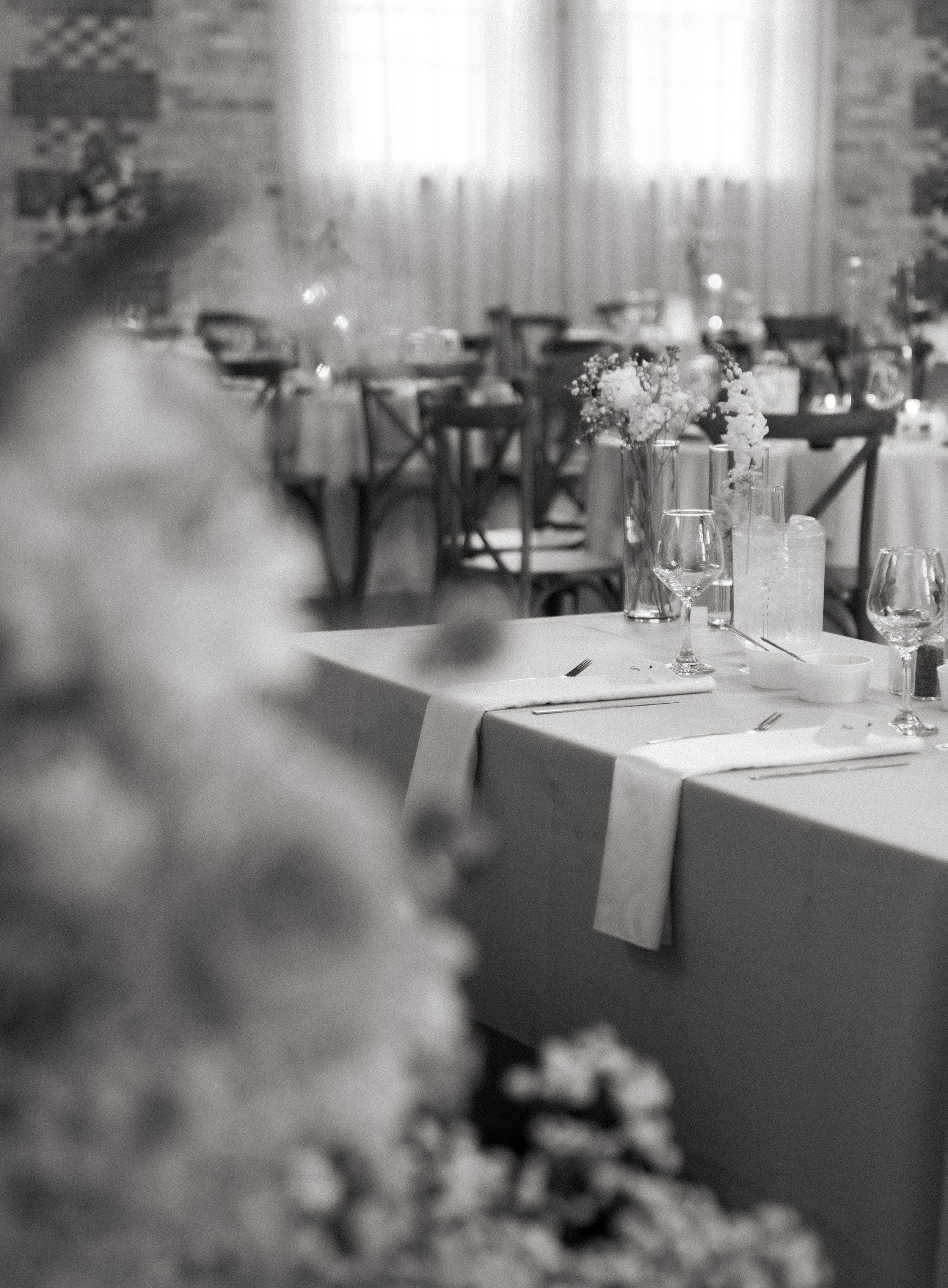 Elegant black and white reception table setting with floral centerpieces and cross-back chairs in a romantic venue.