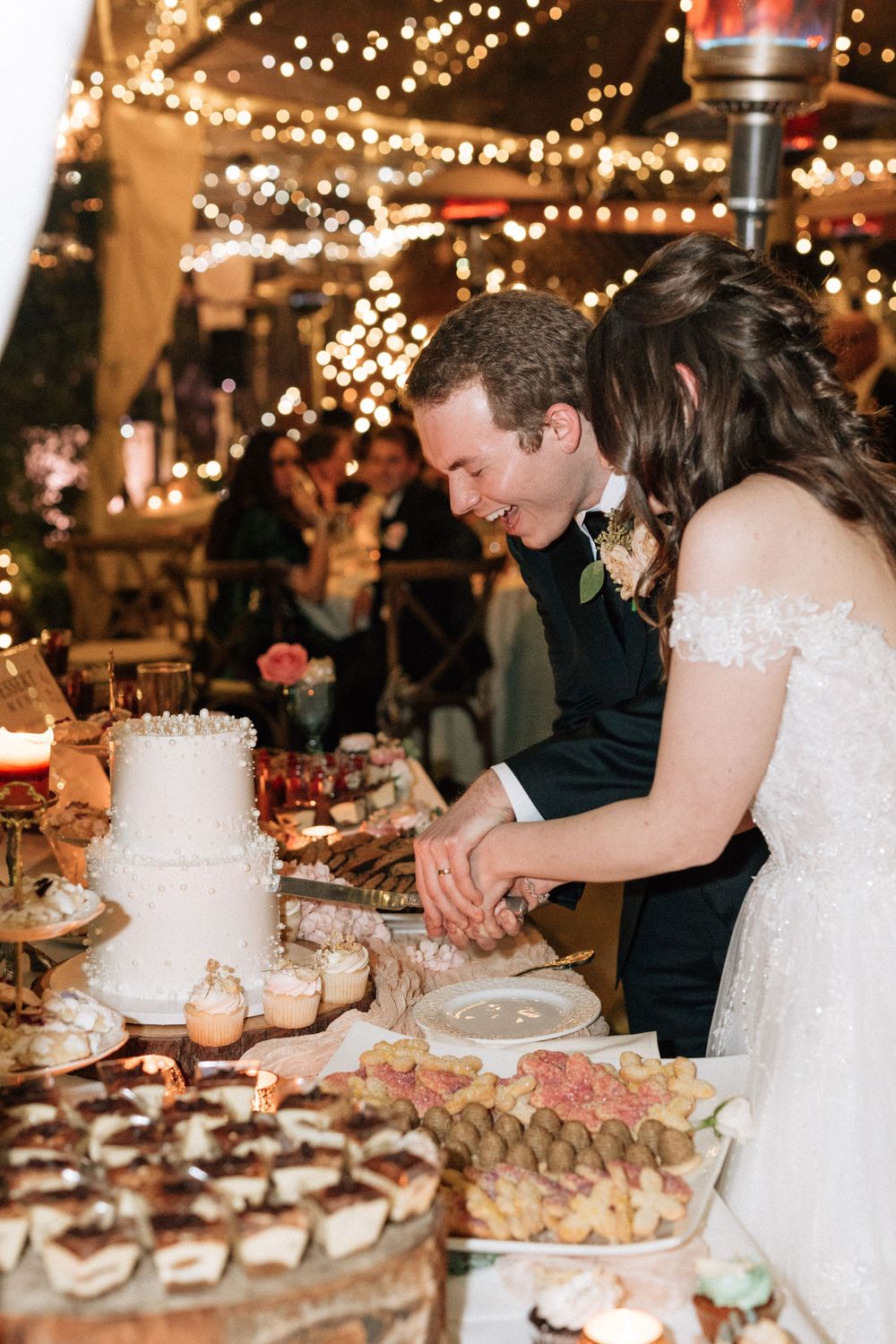 bride and groom cut cake with twinkling lights behind them