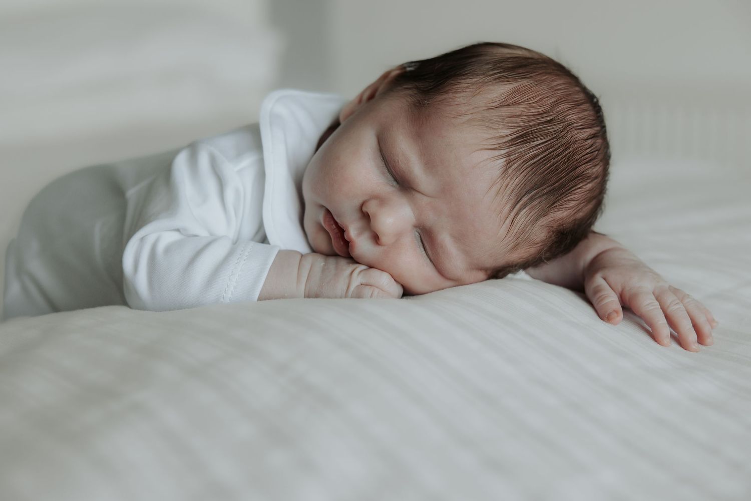 A peaceful sleeping baby in white clothing resting on light-colored bedding.