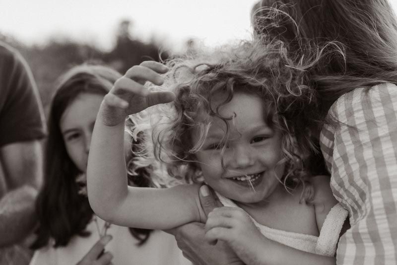 A black and white candid photograph shows a joyous moment filled with natural laughter and curly hair in motion.