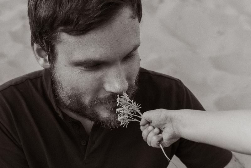 Someone being playfully fed a dandelion flower by another person's hand in a black and white photograph.