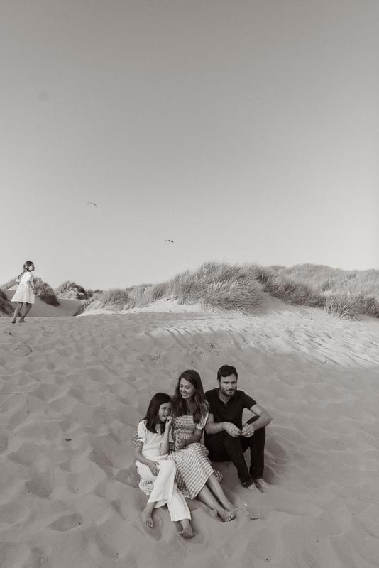 A black and white photograph of people sitting together on sand dunes at the beach on a sunny day.