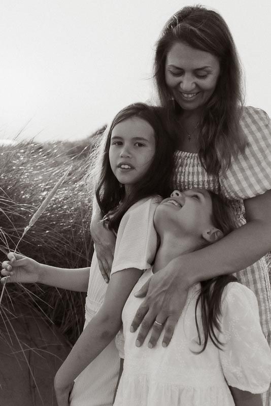 A candid black and white family moment captured outdoors among tall grasses on a sunny day.