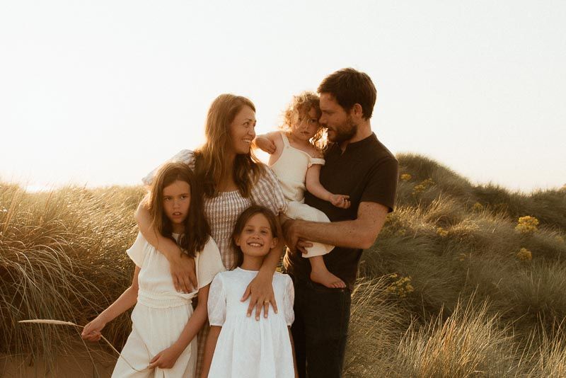 A family stands together in a golden field at sunset with tall grass swaying in the background.
