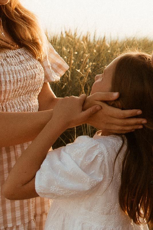 Two people in white dresses share an intimate moment in a sunlit wheat field at golden hour.