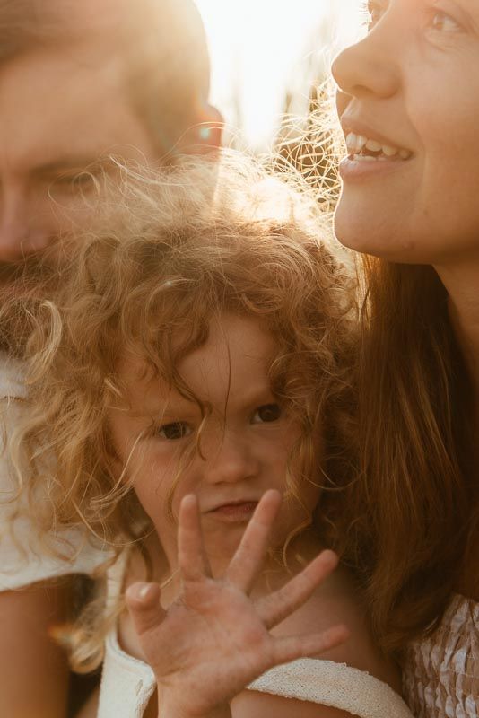 A close-up portrait in warm sunlight showing curly hair and smiling expressions in a tender family moment.