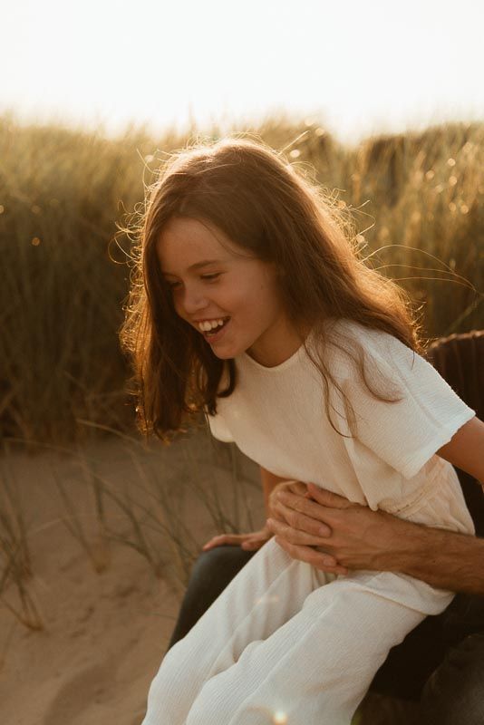 A joyful candid moment captured at sunset, with golden light illuminating long hair and a white t-shirt against a natural backdrop.