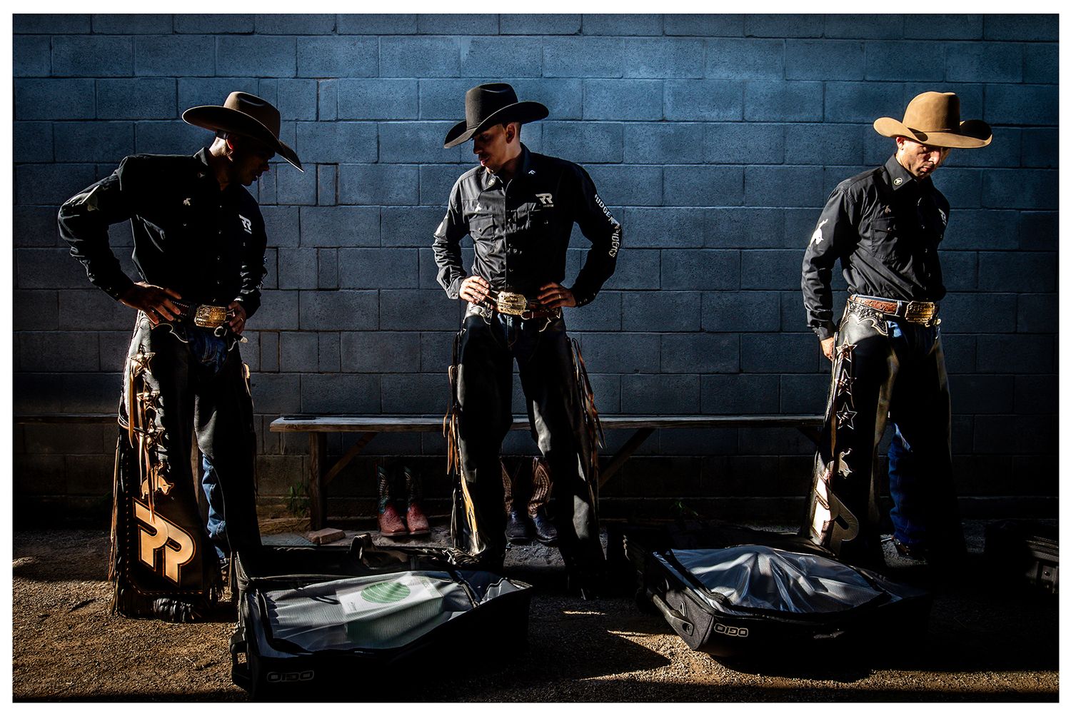 Three Professional Bull Riders getting ready in a locker room that is moodily lit prior to an event photographed by Chris Douglas