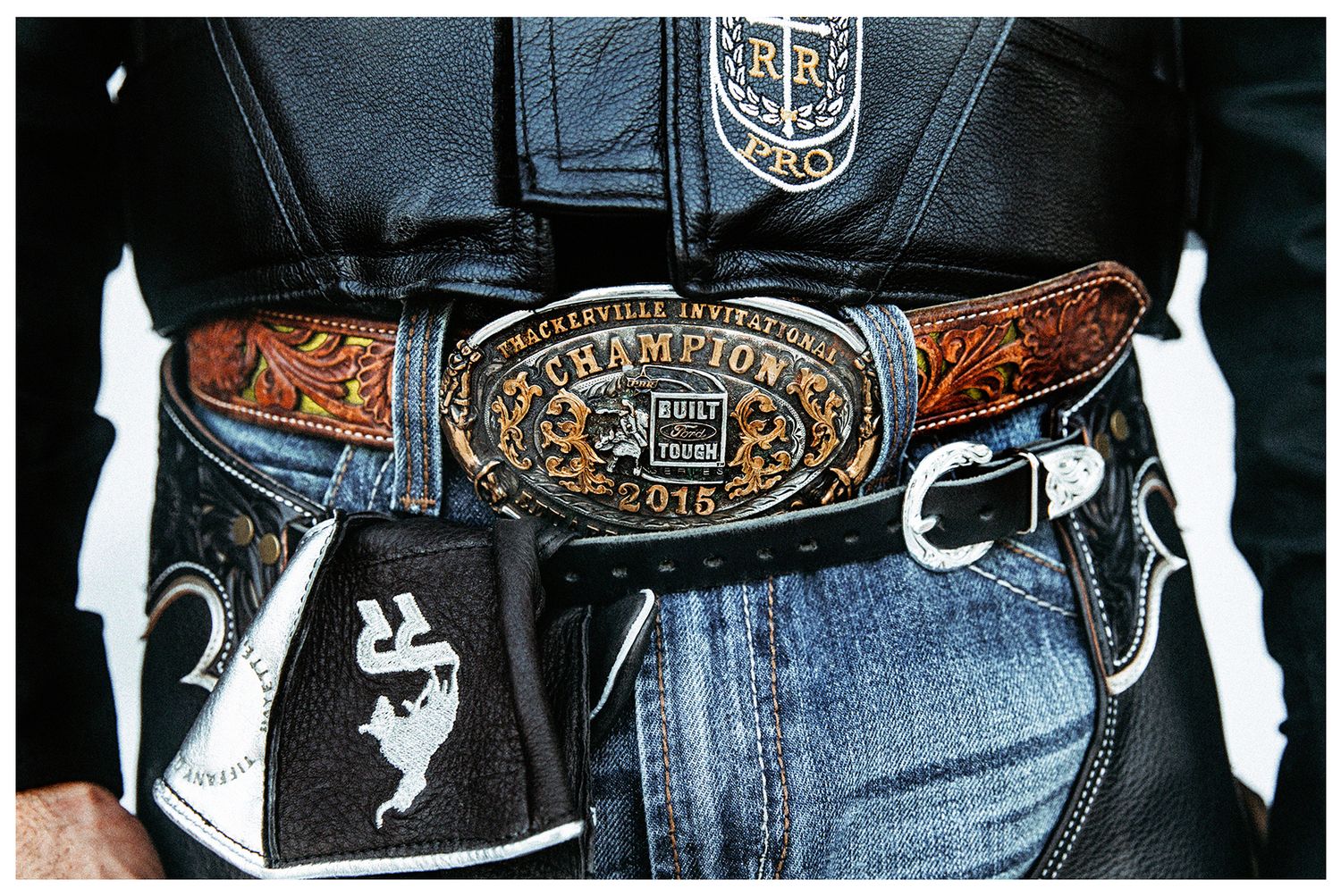 Close up of a PBR buckle with a bull riding vest and a black leather bull riding glove with Ridge Rider Logo photographed by Chris Douglas