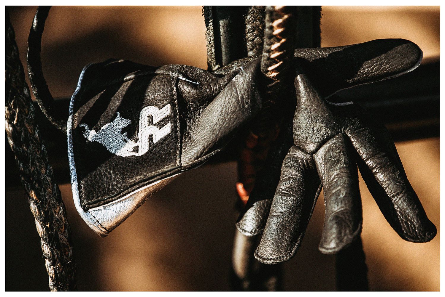 Close-up image of a Arizona Ridge Rider black leather bull riding glove hanging in a bull rope photographed by Chris Douglas