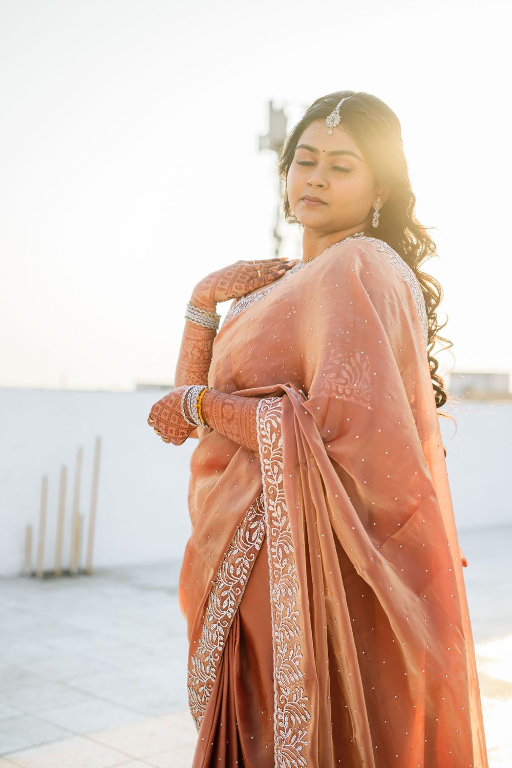 Bridal portrait in peach silk saree with embroidered border against sunset lighting.