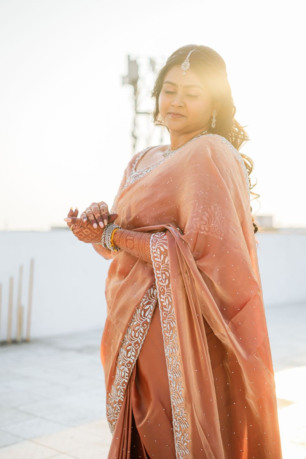 Elegant bridal pose in peach saree with intricate border details during golden hour.