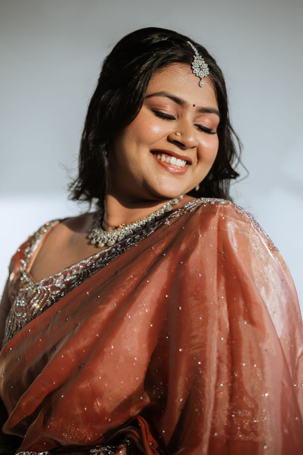 Close-up portrait showing bridal jewelry and peach saree with sparkling details.