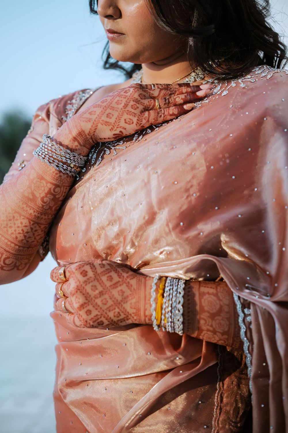 Traditional Indian bridal attire with intricate mehndi designs and bangles in a peachy pink saree.