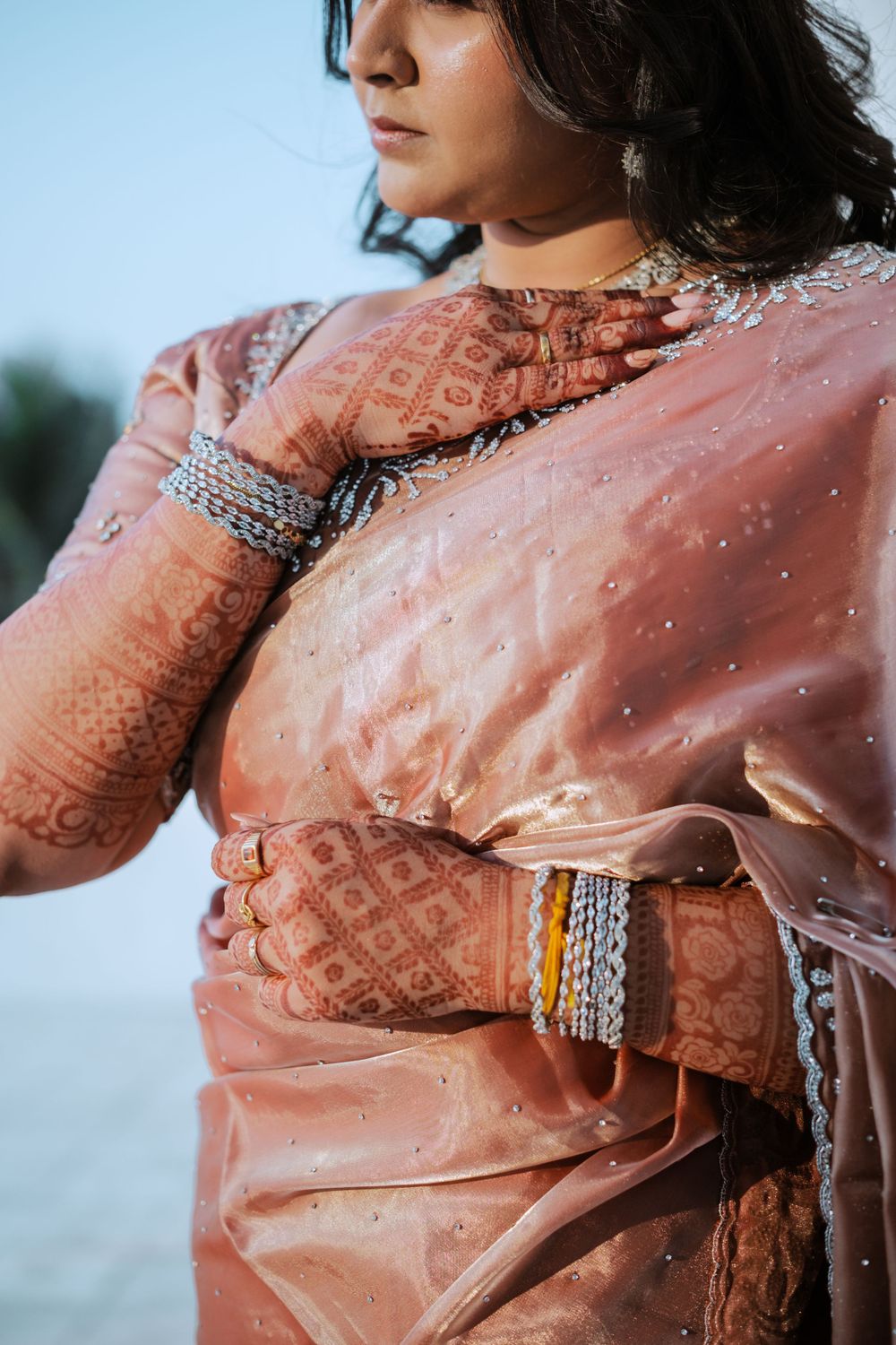 Detailed view of intricate henna designs on hands wearing traditional Indian bangles with peach-colored fabric.
