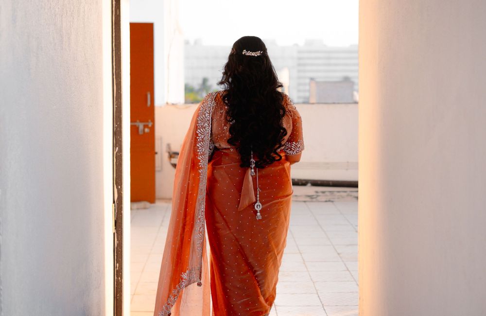 Person wearing an orange sari with chiffon dupatta walks through a bright interior hallway.
