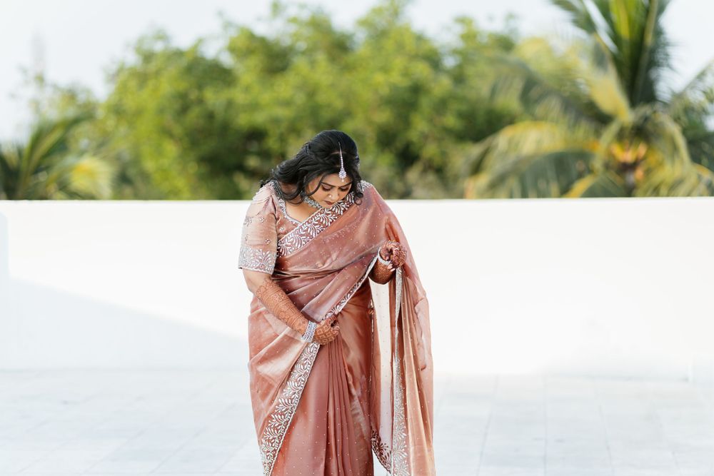 Someone wearing an elegant peach-colored silk saree with embroidery details poses in front of a tropical landscape.