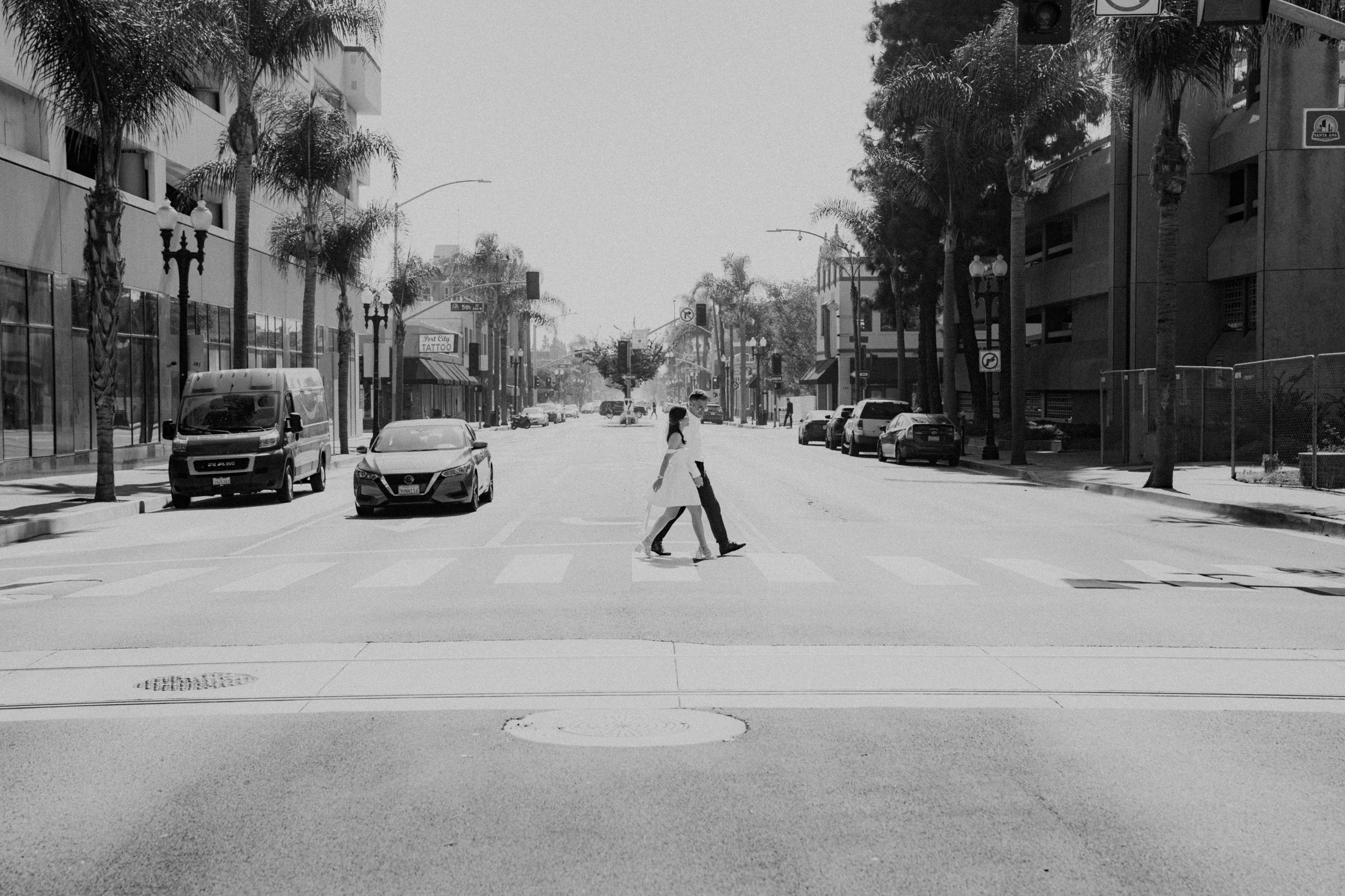 A black and white street scene with palm trees and parked cars along an urban road.