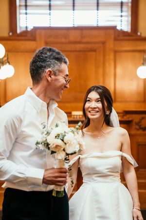 A couple shares a joyful moment during their wedding ceremony with white flowers and wooden paneled walls.