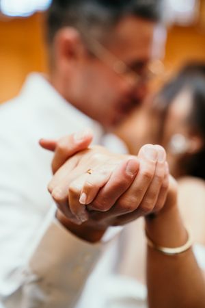Close-up shot of hands clasped together during a wedding ceremony in warm lighting.