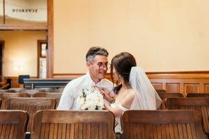 A romantic wedding moment between a couple sitting in wooden church pews with a white bouquet.