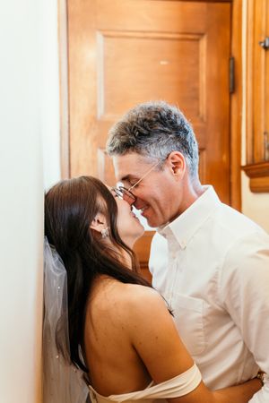 A tender intimate moment with newlyweds sharing a kiss against a wooden door background.