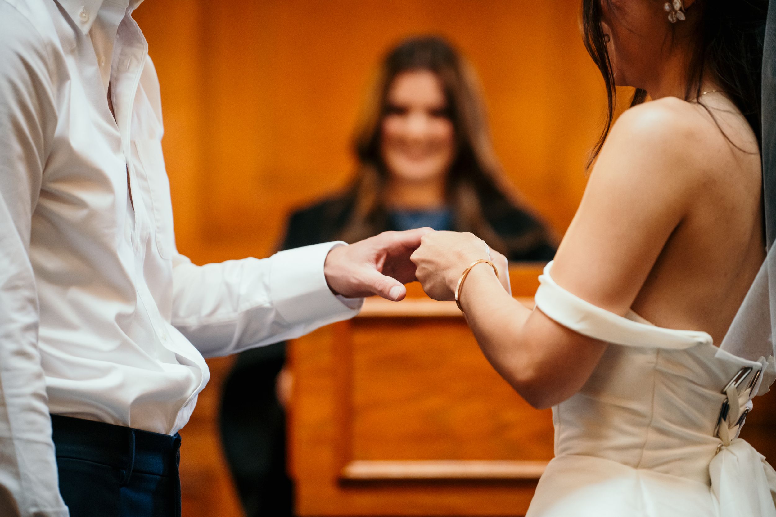 Couple exchanging rings during wedding ceremony with white and orange background.