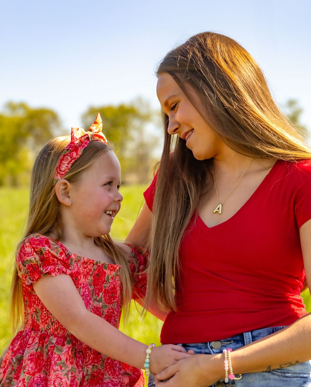 A tender moment shared between two people in red outfits smiling at each other in a sunny outdoor setting.
