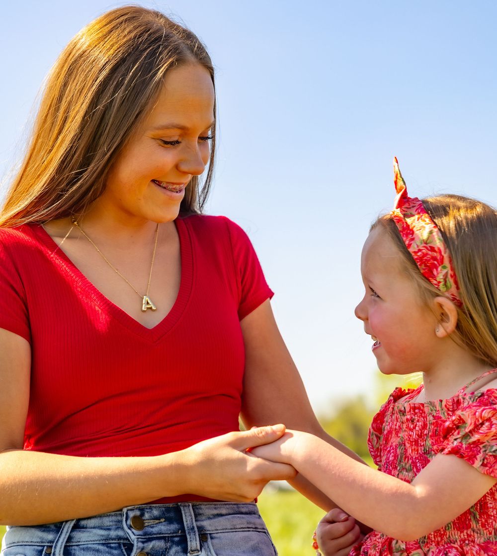 Parent and child in coordinated red outfits share a tender moment while holding hands in sunny outdoor setting.