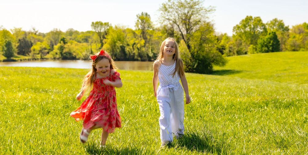 Two people run joyfully through a sun-drenched meadow on a bright spring day.