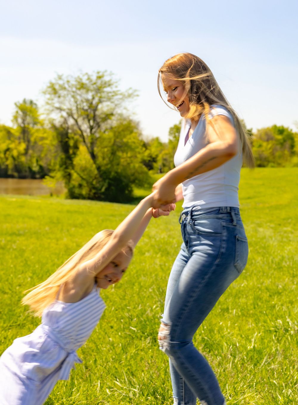Playful moment captured as parent and child spin and dance together in a sunny meadow.