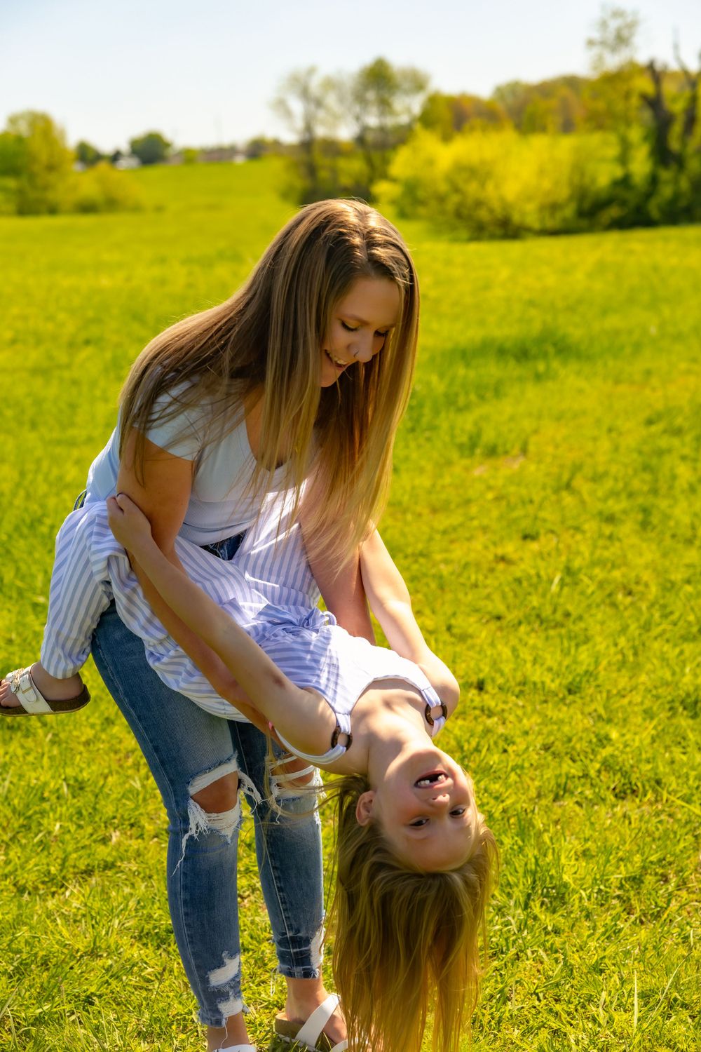 Two people enjoying a playful moment together in a sunny green meadow with trees in the background.