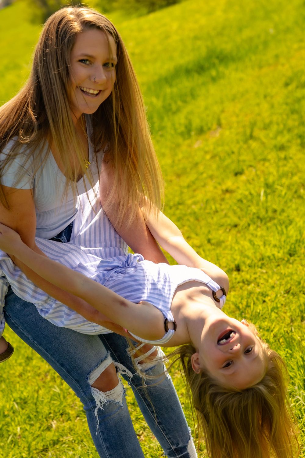Two people playing and laughing together on bright green grass on a sunny summer day.