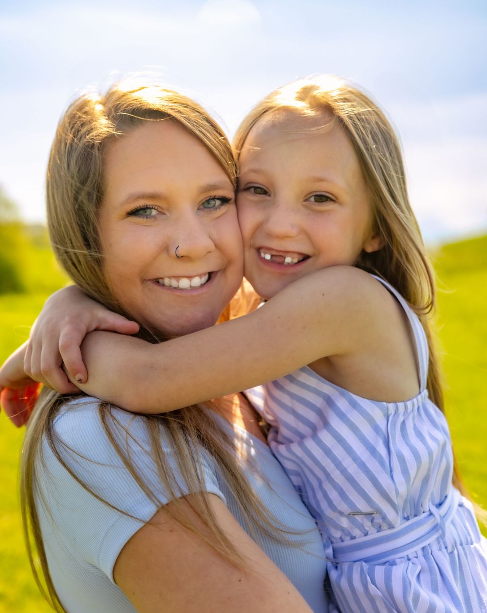 Two people sharing a tender embrace outdoors in warm sunlight with a blurred nature background.