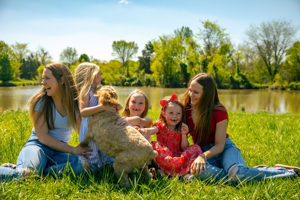 Group sitting together with a dog on grass by a lake on a sunny spring day.
