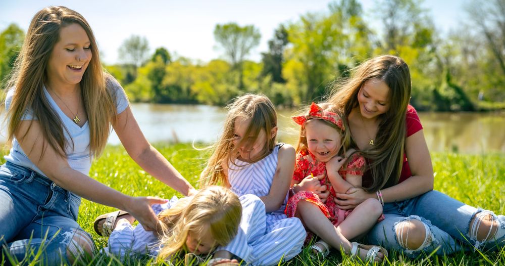 Family group shares laughs while playing with their dog in a sunny field by the water.
