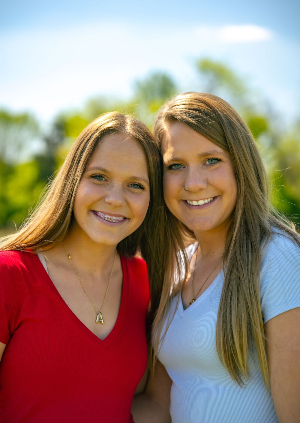 Two people in red and white tops smiling together on a sunny day with green foliage in background.