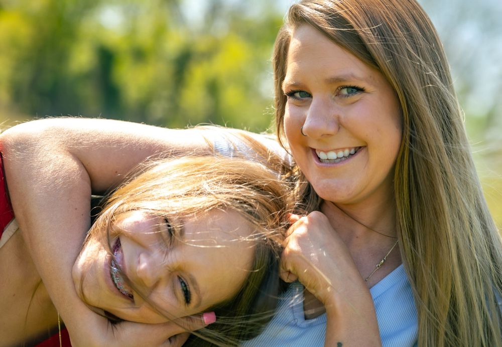 Two people laughing together outdoors with golden sunlight and greenery in the background.