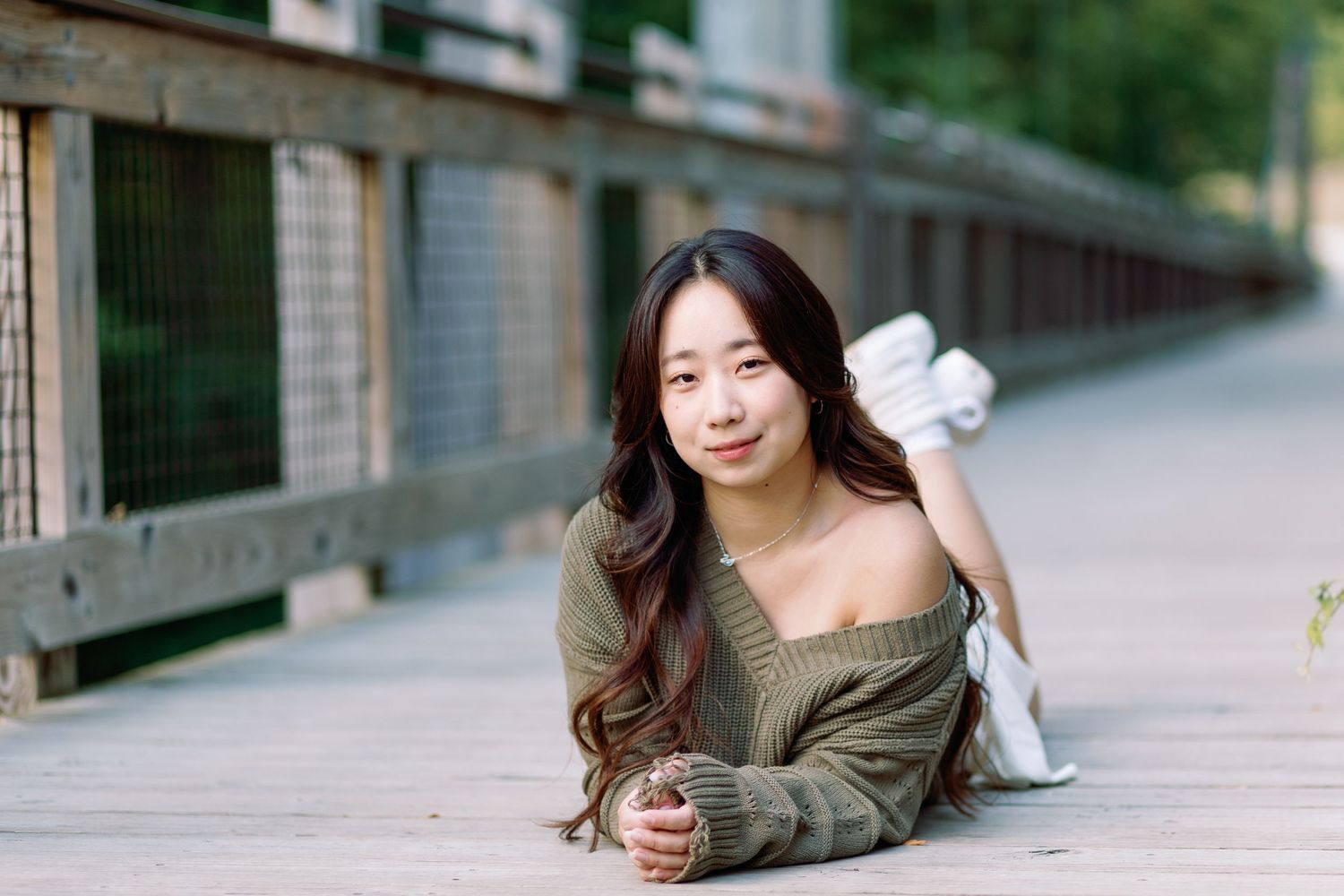 Person in olive green sweater lying casually on wooden boardwalk surrounded by natural scenery.